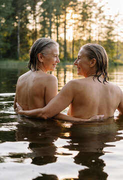 Zwei reife Frauen beim gemeinsamen Wildbaden im See bei Sonnenuntergang