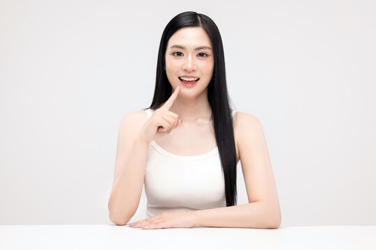 Beautiful Asian woman with clean fresh skin pointing finger at her mouth, smiling with white teeth, beauty skincare and dental care concept, isolated on white background.