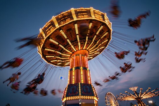 A long exposure photograph of a brightly lit carousel swing ride at a fairground during twilight.