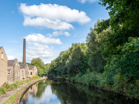The Rochdale canal in Hebden Bridge with houses and trees reflected in the water in summer sunlight