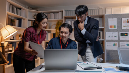 Fototapeta premium Business team discussing work together in office, analyzing reports and data on laptop and documents, showing collaboration, planning, and problem solving during a productive meeting.