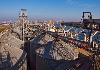 Fototapeta premium Large industrial grain storage facility with conveyor belts and cranes near a waterfront under a clear blue sky