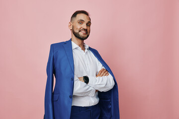A confident business professional stands against a soft pink backdrop, wearing a blue suit draped over the shoulders. He conveys a warm, approachable emotion with a poised posture. © SHOTPRIME STUDIO