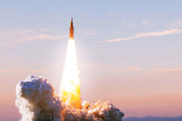Fototapeta premium space rocket launches into the sky at sunrise, leaving thick clouds of smoke and a bright trail of fire behind as it begins its mission. Spaceship lift off to the space Start