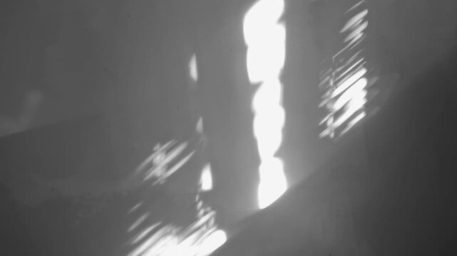 Sunlight reflections and bright glares caustic effects casting abstract shadows on a textured dark wall.