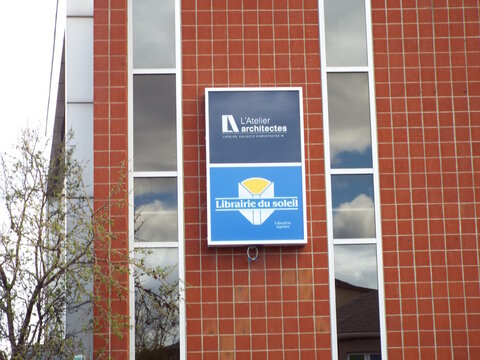 Gatineau, Quebec, Canada &ndash; May 7, 2026: A sign for "L'Atelier architectes" and "Librairie du soleil" hangs on a red-tiled building between windows on Boul Saint-Raymond.