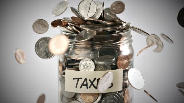 Close-up shot of coins falling in slow motion into a coin jar labeled 'Taxes'.