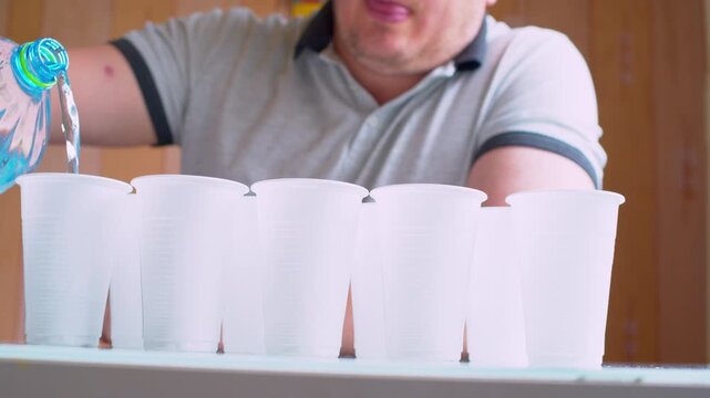 A man pouring drinking water into cups. A cinematic close-up of disposable cups being filled with water. Blurred background. Soft focus, daylight.