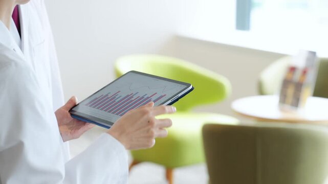 A group of men and women in white coats talking while looking at a tablet.