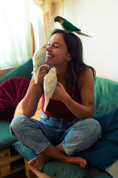 Young woman playing with her pet parakeets at home