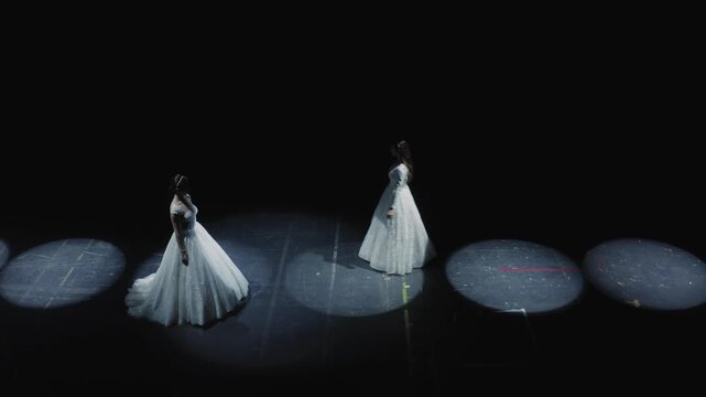 Cinematic wide shot of two elegant models in white wedding gowns posing on dark runway with large circular LED spotlight rings at bridal fashion show. Perfect for wedding, fashion, and luxury content.
