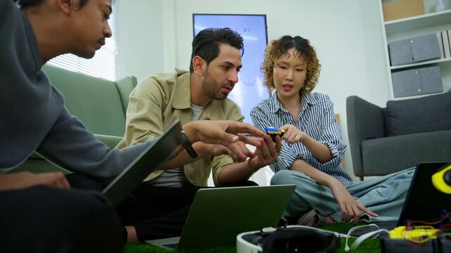 Diverse engineers and developers sitting on grass floor collaborating on agentic AI robotics prototype in modern creative startup workspace. Embedded robotics, IoT development, hardware engineering.
