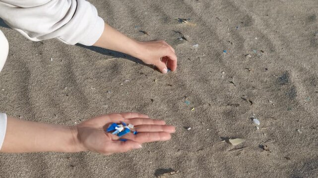 Volunteer picking up microplastics on the beach. Close-up of a volunteer's hands collecting small pieces of microplastic waste from the sand, cleaning the beach to help protect the environment