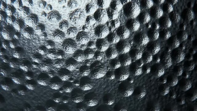 Panning shot of dimpled metal surface with slow moving highlights and reflective light sweep across textured panel in studio interior