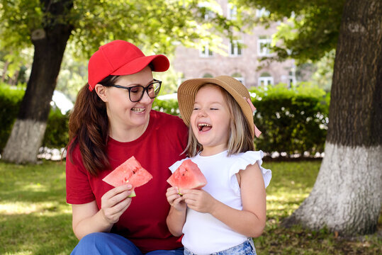Mother and daughter enjoying fresh watermelon in a sunny park, sharing laughter and quality time outdoors. Healthy lifestyle, family bonding, and happy summer moments