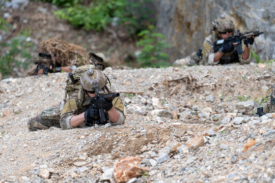 Soldier in camouflage uniform lying in prone position aiming rifle behind rocks. Tactical military warrior holding weapon during combat training outdoor