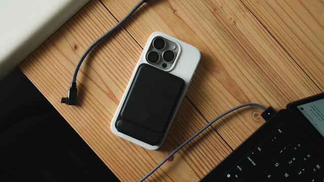 iPhone with MagSafe Battery Pack on Wooden Desk with Laptop and Cable