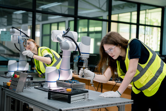 Two women in yellow vests are working on a robot