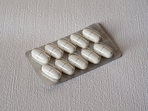 White pharmaceutical tablets in a blister pack placed on a textured light-colored surface. Close-up view of packaged medication, healthcare and medical treatment concept