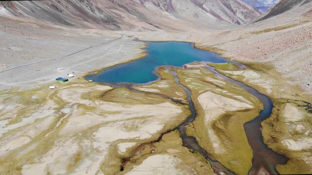 Panoramic orbit shot of blue glacial lake in barren Himalayan valley.