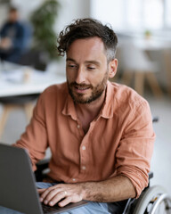 Obraz premium Man in wheelchair uses laptop with calm focus. Soft light highlights his thoughtful expression. Modern office setting suggests productivity and inclusion. Ideal for stories about accessibility