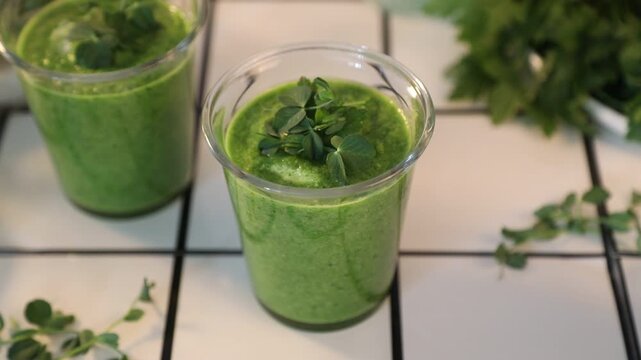 Fresh green gazpacho or smoothie in a glass with herbs microgreens in glass cups on a light background