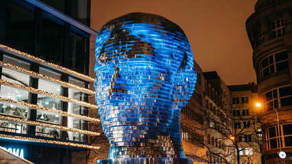 Obraz premium Prague, Czechia - 20.12. 2025. Night timelapse of rotating Franz Kafka Head sculpture. illuminated with shifting colorful lights. Striking kinetic art installation