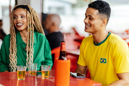 Brazilian friends enjoying drinks and watching football together at a casual bar, celebrating and socializing in a vibrant atmosphere.