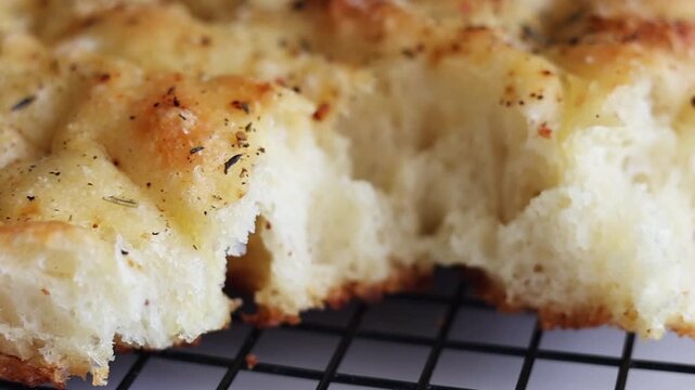 Macro shot panning across the golden crust of freshly baked Italian focaccia bread topped with herbs, salt, and spices. Detailed view of the textured surface showing rosemary, pepper, and seasonings o