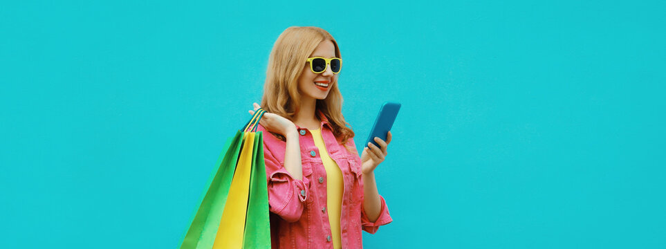 Beautiful happy young woman looking at phone with shopping bag, stylish girl holding smartphone