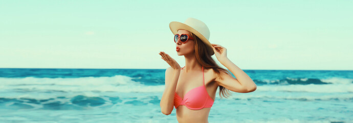 Fototapeta premium Summer vacation, beautiful young woman blowing kiss in bikini swimsuit, tourist hat on beach on sea