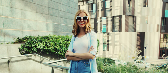 Beautiful modern young woman looking at camera standing on city street in summer wearing glasses © rohappy