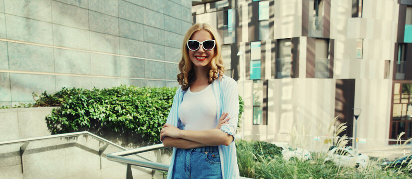 Beautiful modern young woman looking at camera standing on city street in summer wearing glasses