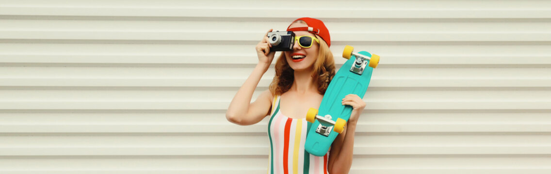 Summer happy cheerful stylish young woman with skateboard takes picture with camera on white