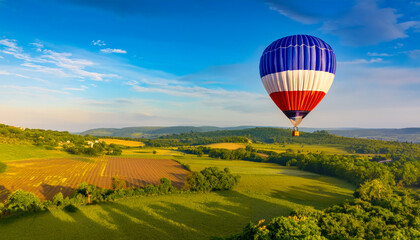Fototapeta premium Hot Air Balloon Floats Over Hills and Fields in a Sunny Landscape During the Morning