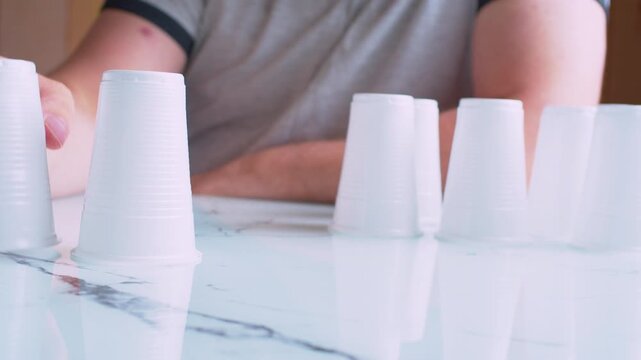 Cinematic macro shot of stacking plastic cups on a table. Blurred man silhouette. Soft focus, bokeh, natural light. 