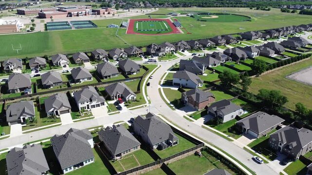 School adjacency view in Arlington, TX shows curved residential streets leading toward large campus with fields, courts brick buildings shaping shared community edge. Clear proximity between homes
