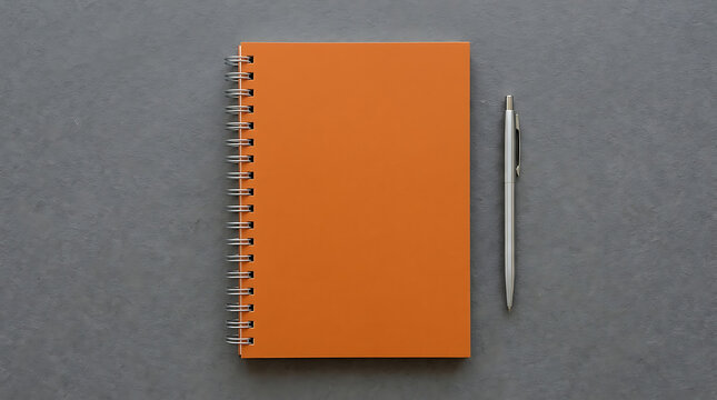 Vibrant orange spiral notebook featuring a blank cover for creative mockup design lying on a textured dark gray paper surface representing modern stationery planning education and organization.