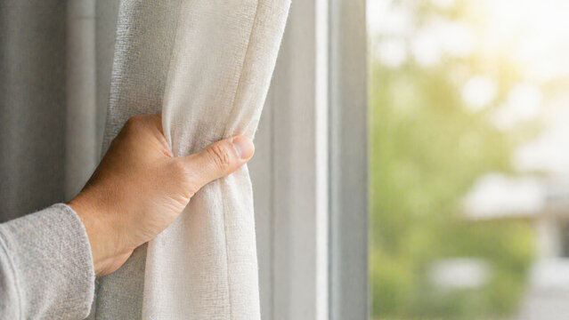 Hand opening curtain to let natural light in, representing fresh start, morning routine, and home lifestyle