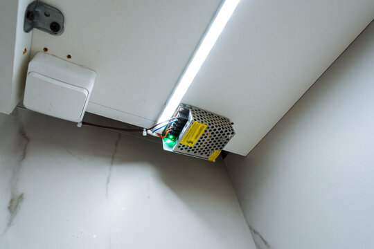 Lighting setup overview. Shelf lighting connector with LED strip and junction box. Technical image showing cabinet lighting junction box and LED strip illumination on tiled wall