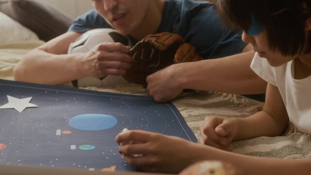 Young man and child playing with solar system map and space toys. Ideal for STEM education marketing, parenting campaigns, and family lifestyle advertisements