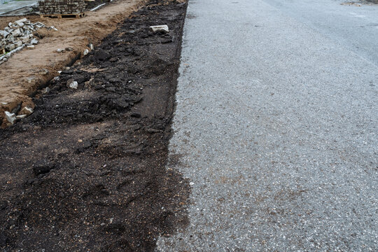 Sidewalk trench excavation. Workers ready surface by clearing dirt and debris for paving. Excavation work exposes soil and debris while preparing foundation for paving stones