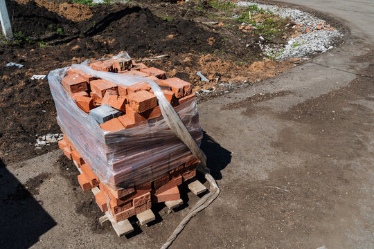Pallet Of Bricks Roadside Assembly. Urban DIY Project With Chipped Brick Units. Masonry Supplies Consisting Of Red Bricks On Pallet With Damaged Wrapping Ready For Building Repairs