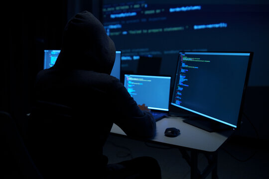 Hacker in Hoodie Working on Multiple Code Monitors