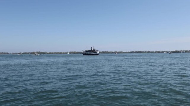 Fixed view of Toronto Inner Harbour on a busy early summer day. Passenger vessels, water taxis, recreational boats and an aircraft move across Lake Ontario under clear skies.
