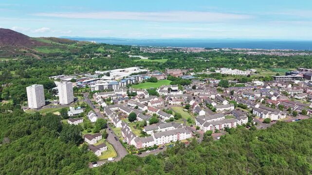 Cinematic aerial drone forward flight over the Greendykes residential neighborhood in Edinburgh, Scotland. Beautiful suburban cityscape view stretching to the sea coast on a summer day.