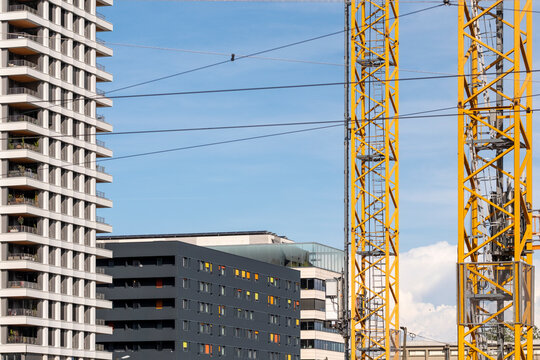 Yellow crane towers across residential blocks and city buildings, framing construction site, windows and urban development against pale sky