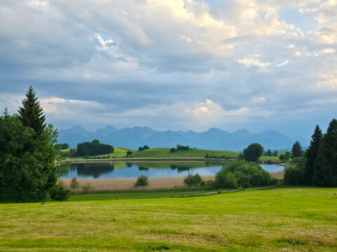 germany, breathtaking lake reflections across green pastures with alpine panorama under bright summer cloud formations