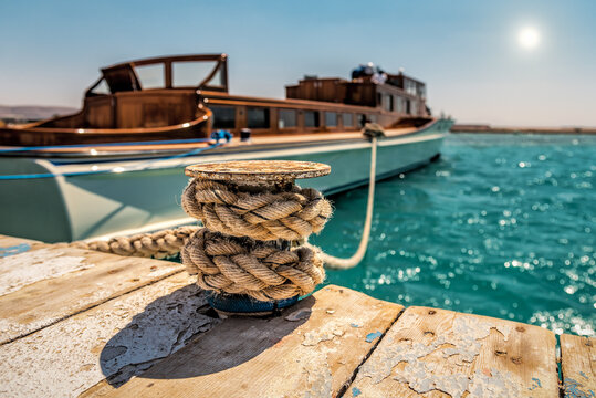 Close-up of a wooden pier with a bollard and ropes against the background of a luxury yacht. Travel and vacation theme