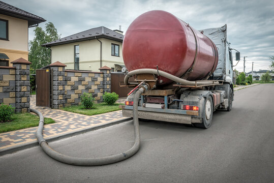 Red sewage vacuum truck pumping out a septic tank through a long hose at a residential suburban house.